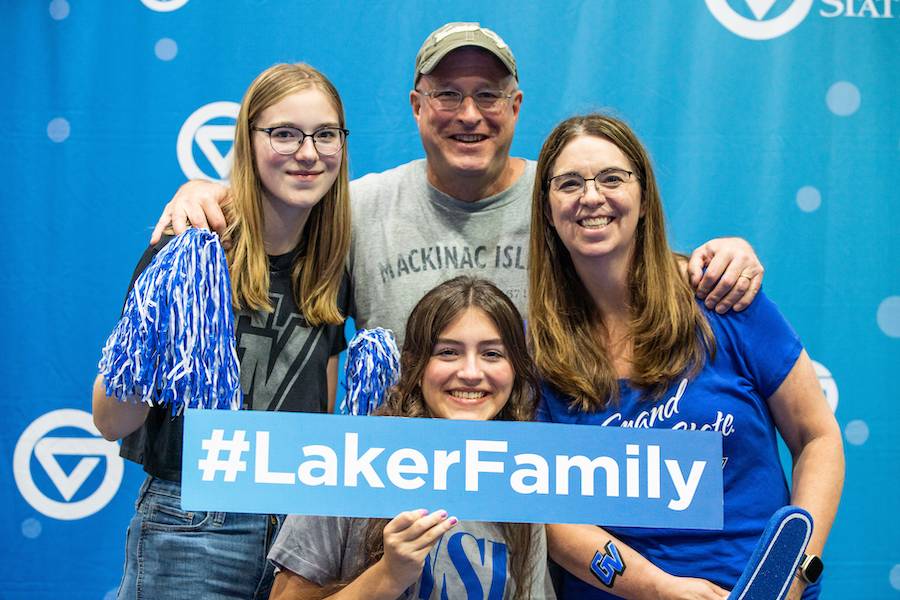 A family taking a photo while holding a Laker Family sign